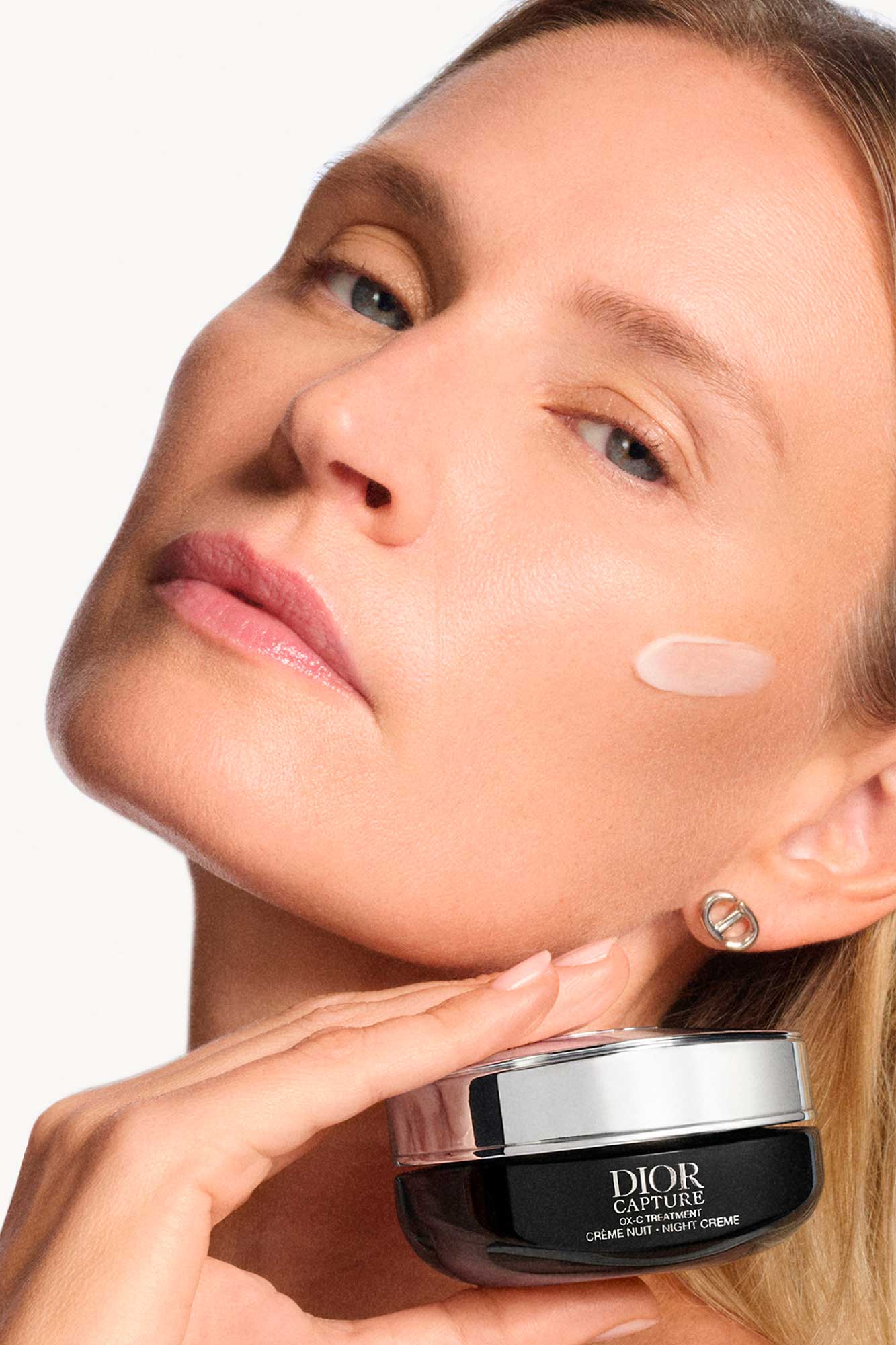 Retrato de uma mulher aplicando o creme noturno antienvelhecimento Dior Capture nas maçãs do rosto